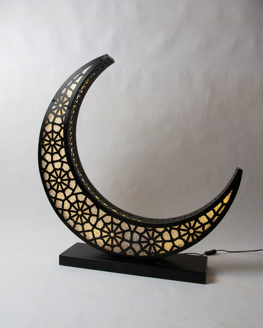 Decorative lamp shaped like a crescent moon with intricate cut-out patterns on a white background