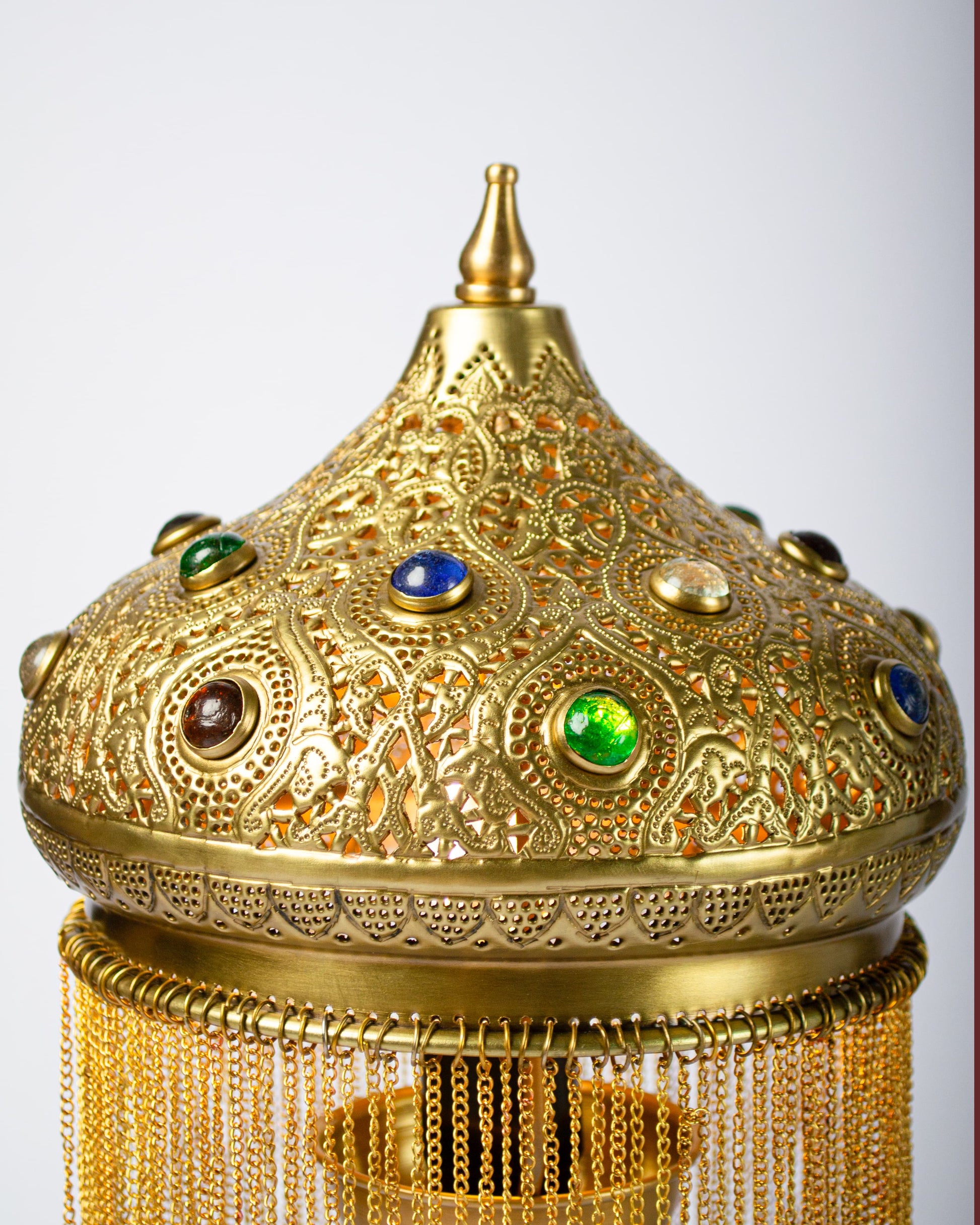 Decorative gold object with intricate designs and colored stones on a white background